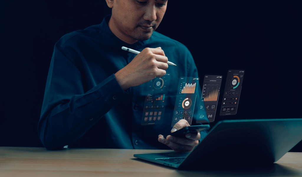 Gentleman on a laptop with a stylus, looking at his phone with hologram dashboards coming off the phone.