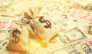 Bags of gold with dollar signs on them, sitting on varying global currencies.